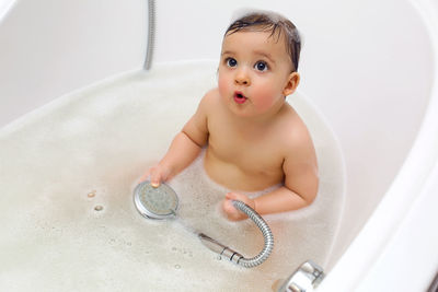 Baby boy sitting in bath with water and foam