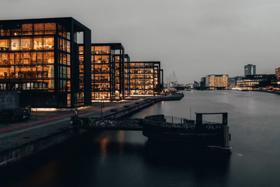 Buildings by river against sky at dusk