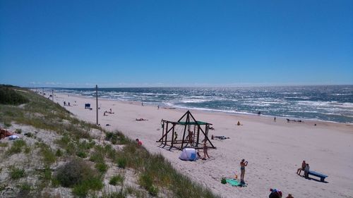 People at beach against clear blue sky during sunny day