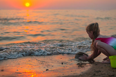 Little blonde girl builds a sand castle on the seashore in at sunset in the golden hour in summer