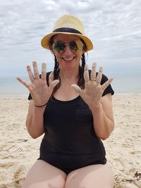 Portrait of smiling young woman showing sand covered hands at beach