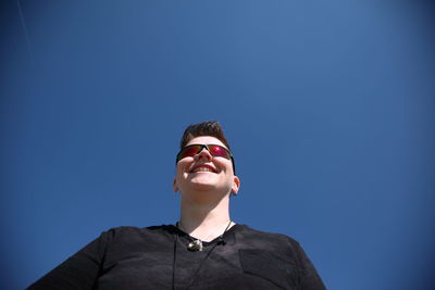 Low angle view of happy woman against clear blue sky