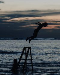 Full length of silhouette girl diving into sea during sunset