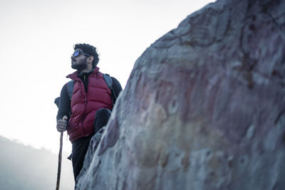 Young indian traveler hiking up the mountain with a backpack and a stick, with a beautiful lake.