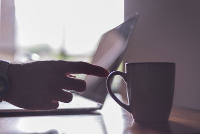 Cropped hand of man picking coffee cup on table at office