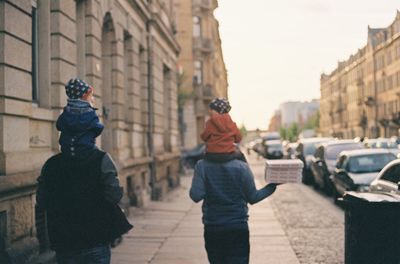 Rear view of people walking on street amidst buildings in city