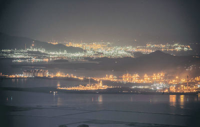 Illuminated city by sea against sky at night