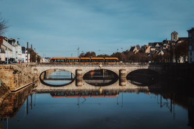 Bridge over river by buildings against sky in city