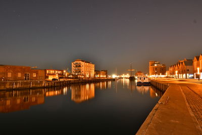 Illuminated buildings by river against sky at night