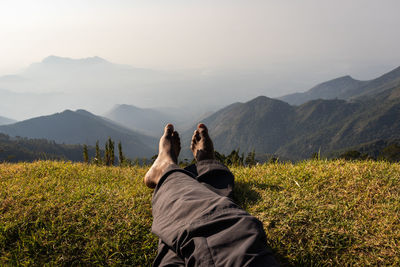 Low section of person relaxing on mountain against sky