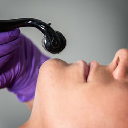 Close-up of woman lying down with while beautician using cosmetic roller on face at spa