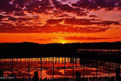 Silhouette trees by lake against dramatic sky during sunset