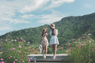 Rear view of women standing on flowering plants against sky