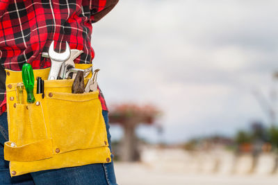 Midsection of man wearing tool belt while standing against sky