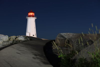 Lighthouse by illuminated building against sky at night