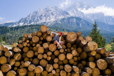 Woman sitting on the stack of the tree logs