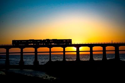 Silhouette bridge over sea against sky during sunset