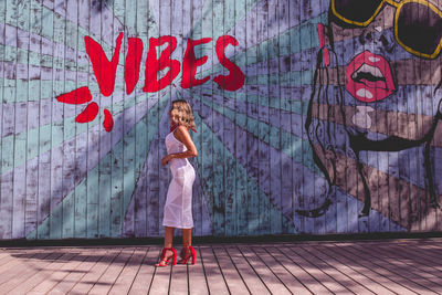 Full length of woman standing against graffiti wall