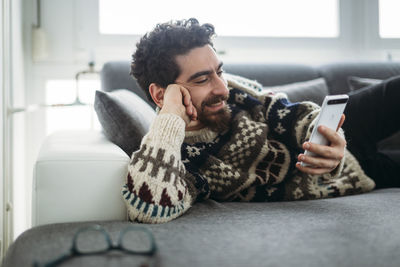 Smiling man lying on a couch looking at phablet