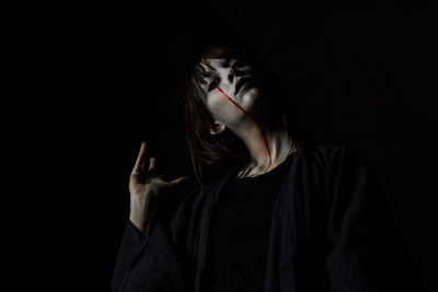 Portrait of young woman with halloween make-up against black background