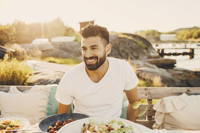 Smiling young man having lunch at party on jetty during sunny day