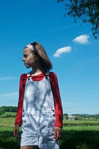 Girl looking away while standing on field against blue sky