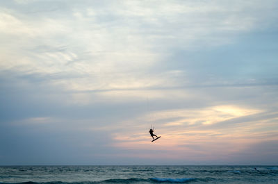 Distant view of silhouette man kiteboarding over sea against cloudy sky