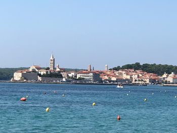 Sailboats in sea by buildings against clear blue sky