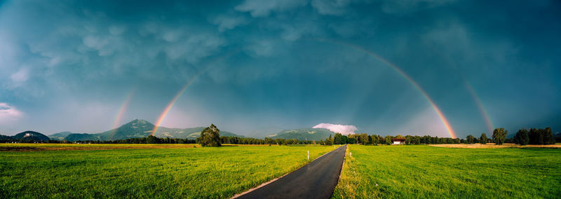 Panoramic image of glowing double rainbow above fields and road in salzburg, austria