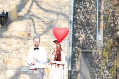 Rear view of couple holding heart shape balloons