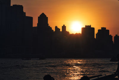 Silhouette buildings by sea against sky during sunset