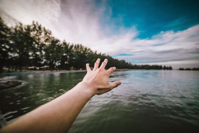 Cropped hands of person reaching sky against sea