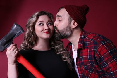 Man kissing girlfriend holding axe by red wall