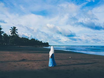 Woman standing at beach against cloudy sky