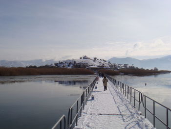 Rear view of woman walking on snow covered pier over lake against sky