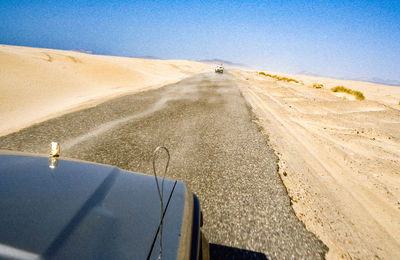 Road amidst desert land against clear sky