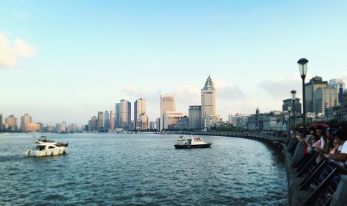 People standing on promenade by river with city in background against sky