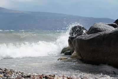 Waves splashing on rocks at shore against sky