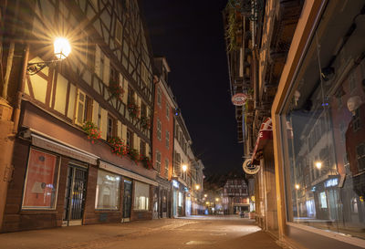 Illuminated street amidst buildings against sky at night