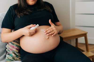 Unrecognizable pregnant woman creams her belly.