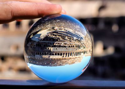Close-up of hand holding crystal ball against coliseum