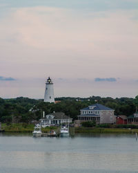 Lighthouse amidst buildings and sea against sky