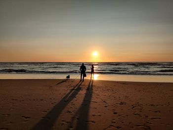 Silhouette people on beach against sky during sunset