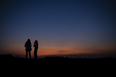 Silhouette people standing on land against sky during sunset