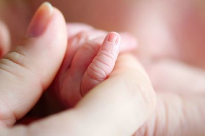 Cropped image of mother and baby holding hands at home