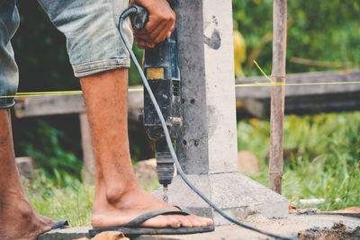 Low section of male worker drilling by column on field