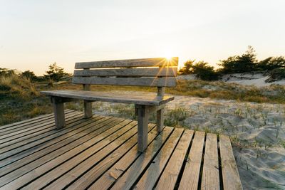 Empty bench by walkway against sky during sunset