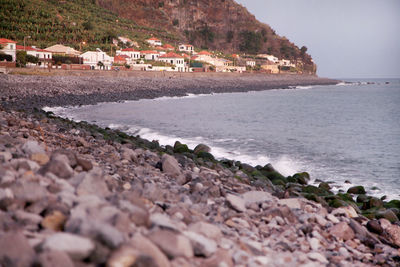 Stones on shore with buildings and mountain in background