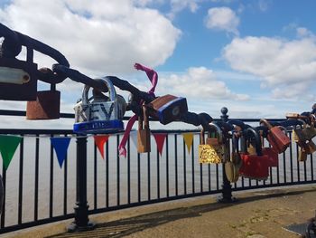 Padlocks hanging on railing by lake against sky