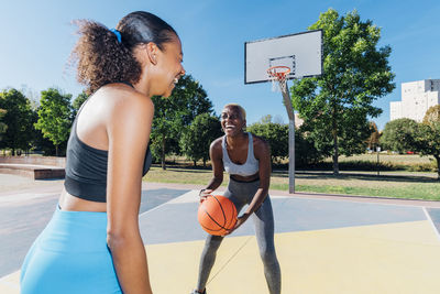 Happy sportswomen playing basketball in court on sunny day